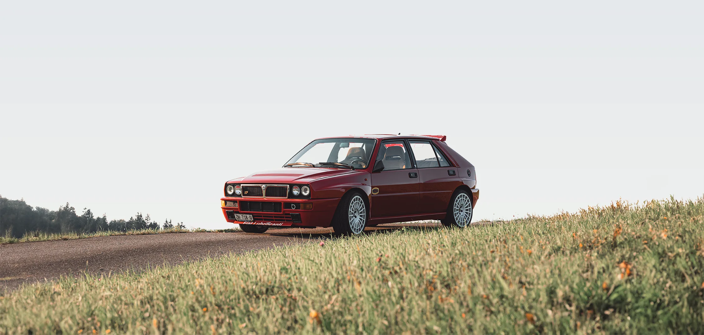 Roter Lancia Delta am Rand einer Landstrasse mit Wiese im Vordergrund